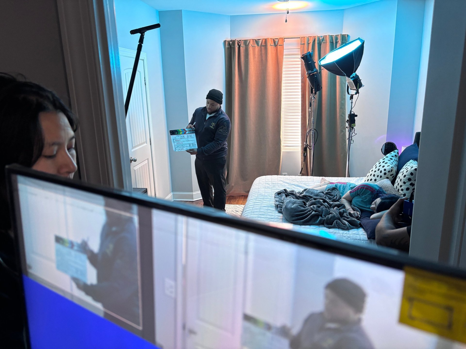 Behind-the-scenes view of a photo or video shoot with crew members, professional lighting, and models on a studio set