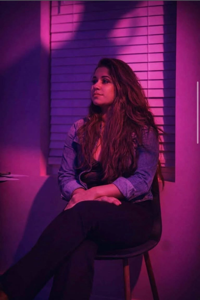 Woman with long dark hair sitting on chair against neon pink and purple lit wall