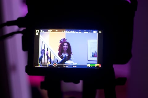 Smartphone screen displaying a woman with curly hair wearing a tiara, held up in purple-lit environment