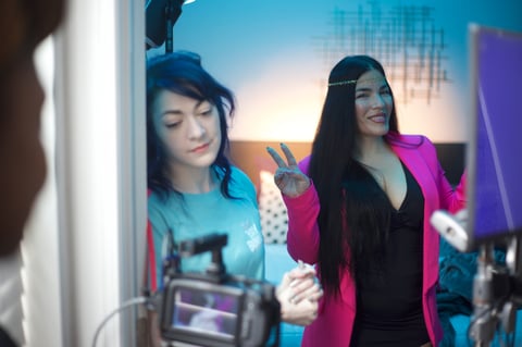 Two women in a tech setting, one wearing blue and one in a pink blazer, looking at digital displays and equipment in a modern workspace