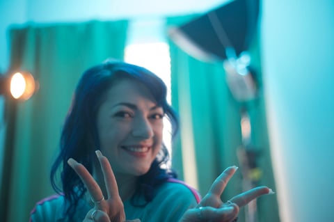 Woman with hands raised smiling in turquoise-lit indoor setting with warm lighting
