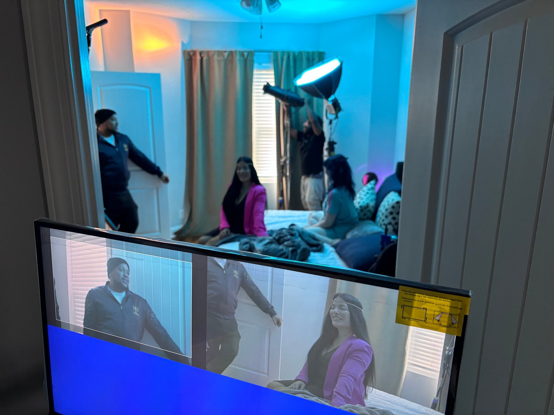 View of people in a blue-lit room with video conference participants displayed on a lower screen in the foreground