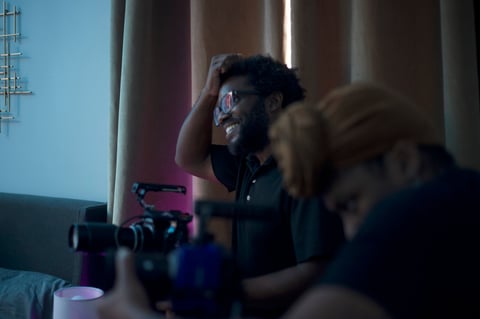 Person wearing headphones in a dark room with blue lighting, sitting at a desk with equipment and another blurred figure nearby